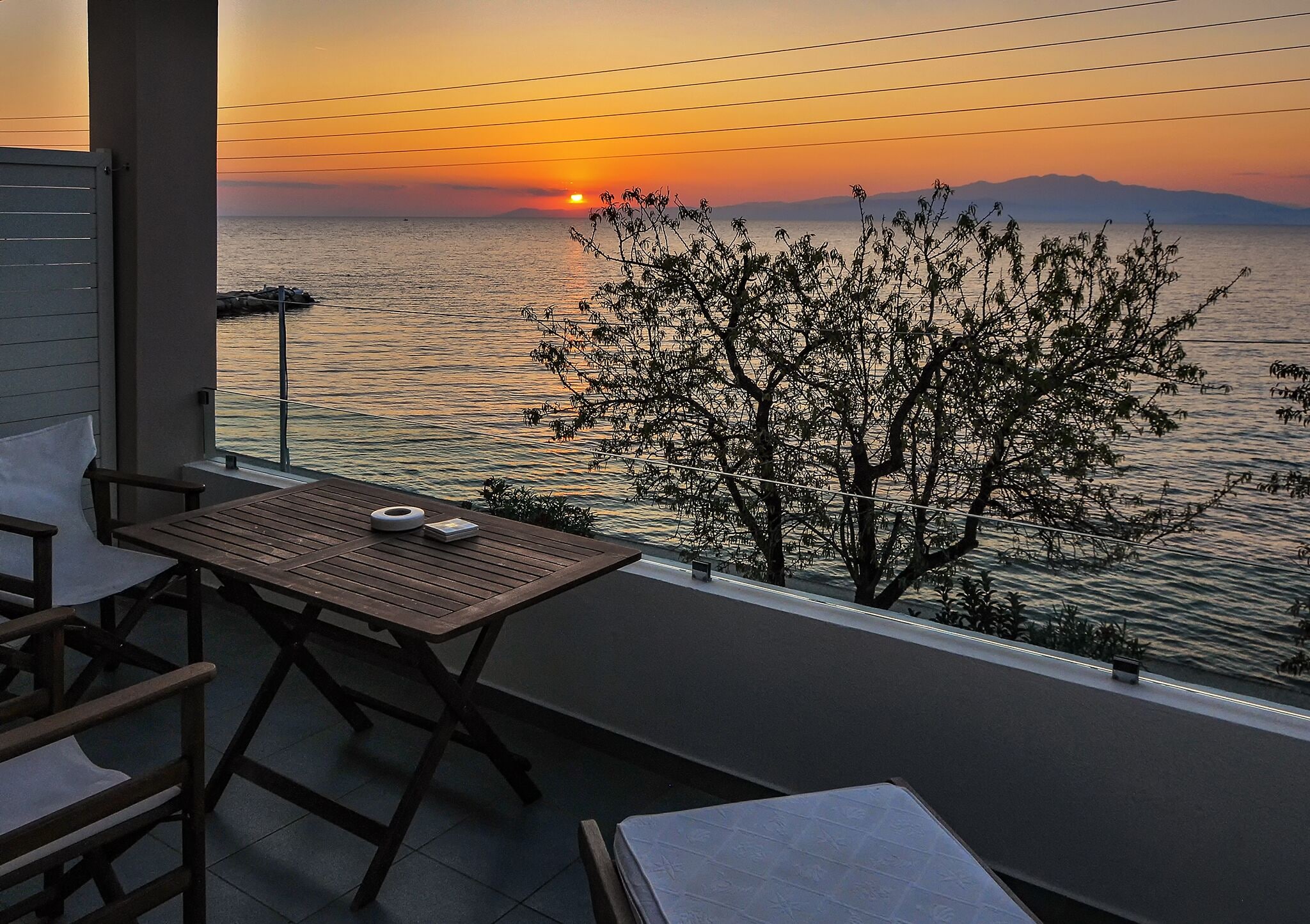 Ein Balkon mit Blick auf den Sonnenuntergang über dem Wasser, ein Tisch und Stühle.