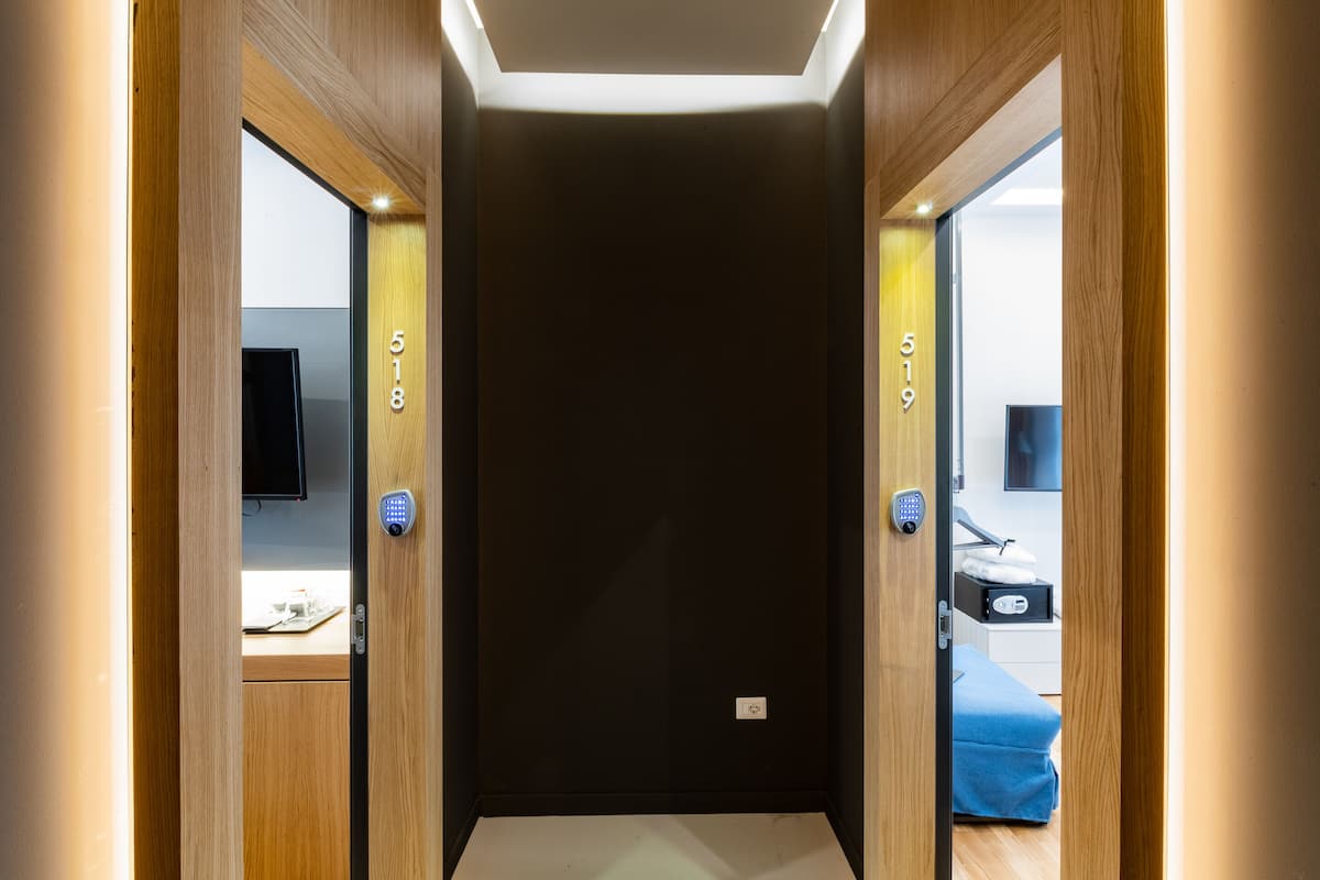 A hallway with wooden walls and a dark floor, leading to a room with a bed and a desk.