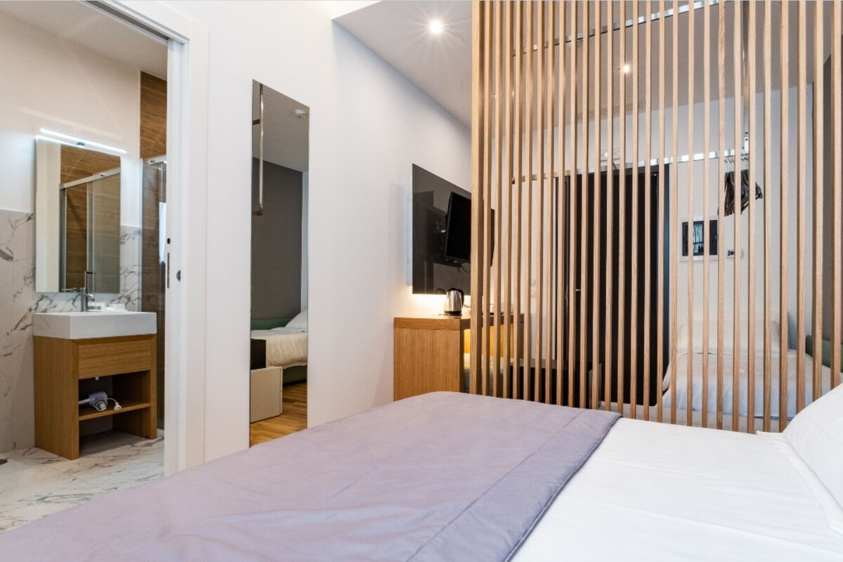 Un dormitorio moderno con cama, mesita de noche, espejo y televisor.