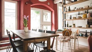 A dining area with a wooden table and chairs, a potted plant, and a kitchen with shelves and cabinets. - The Hostello (Verona)