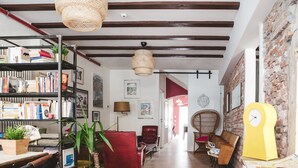 A spacious living area with exposed wooden beams, a bookshelf filled with books, a red armchair, and a yellow clock. - The Hostello (Verona)