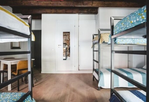 A room with bunk beds, a wooden floor, and a white door with a small window. - The Hostello (Verona)