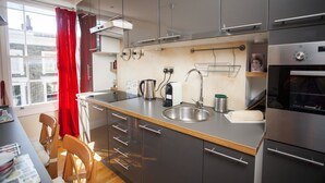 A modern kitchen with grey cabinets, a stainless steel sink, a kettle, a coffee maker, and a built-in oven. - Camden Town Colorful Market Atmosphere (London)