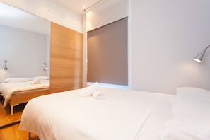 A modern hotel room with a large bed, a bedside table, a mirror, and a window with a view.