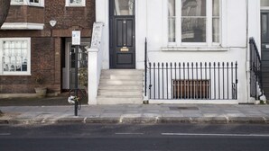 A two-story townhouse with a black front door, white trim, and a small front yard with a metal fence. - Chelsea for History and Art Lovers (London)