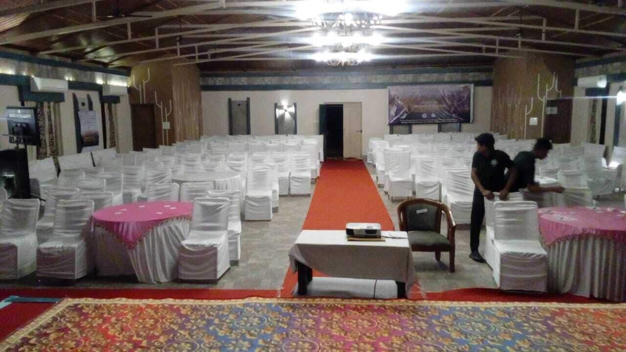 Un salón amplio con filas de sillas blancas, una alfombra roja y una mesa con mantel rosa.