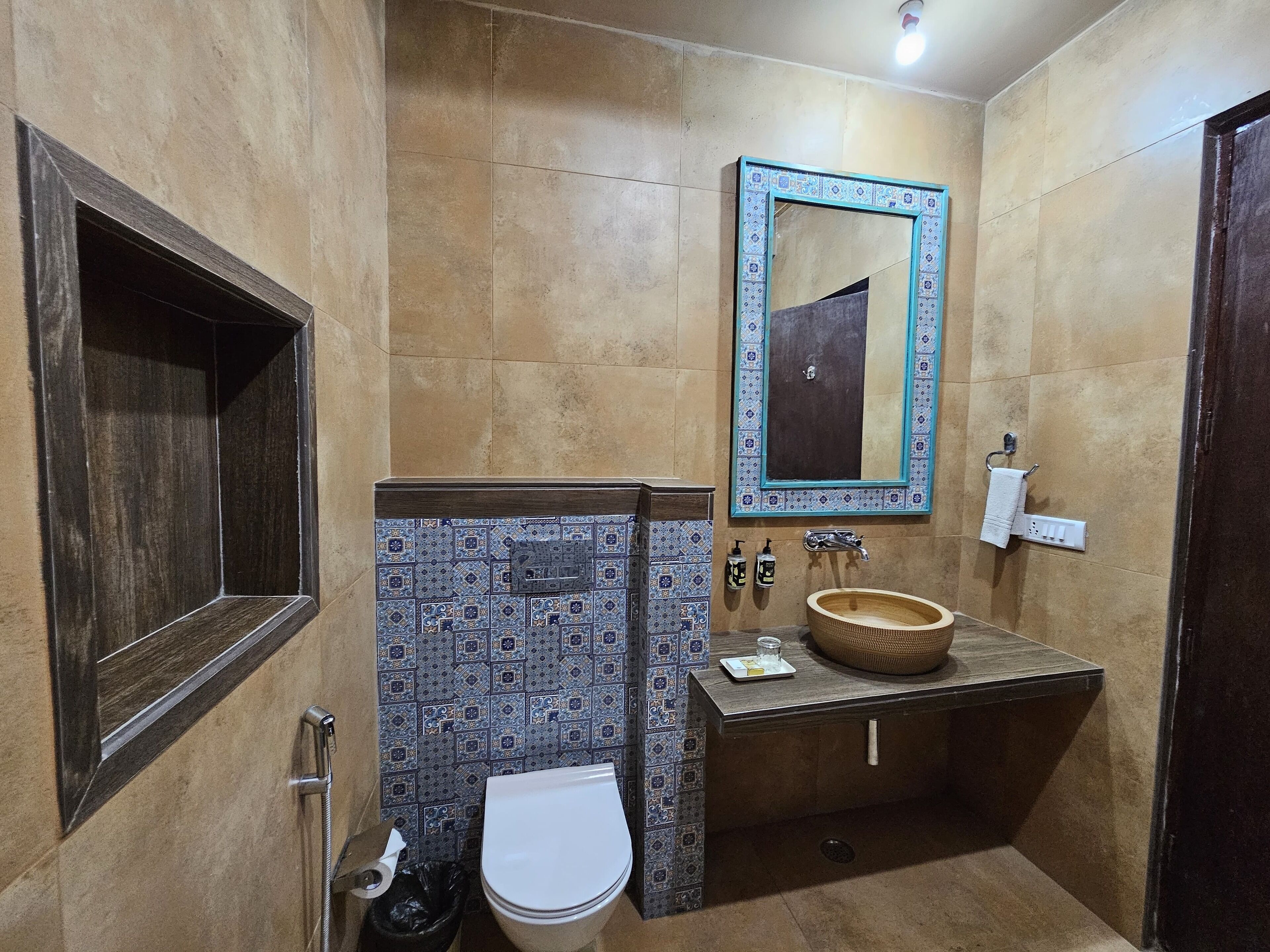 A bathroom with a white toilet, a wooden vanity with a bowl sink, a mirror with a blue frame, and a patterned tile backsplash.