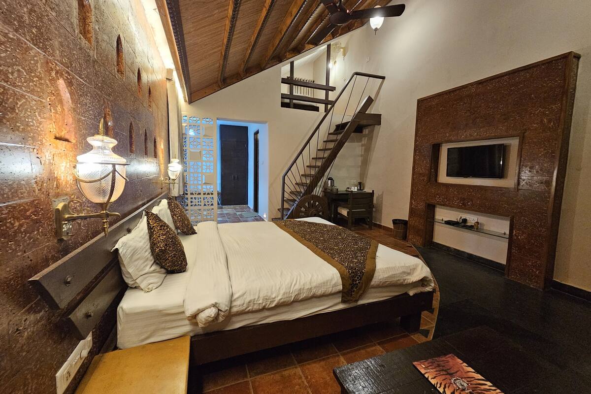 Une chambre à coucher avec un grand lit, un plafond en bois, un escalier, une télévision et un luminaire fixé au mur.