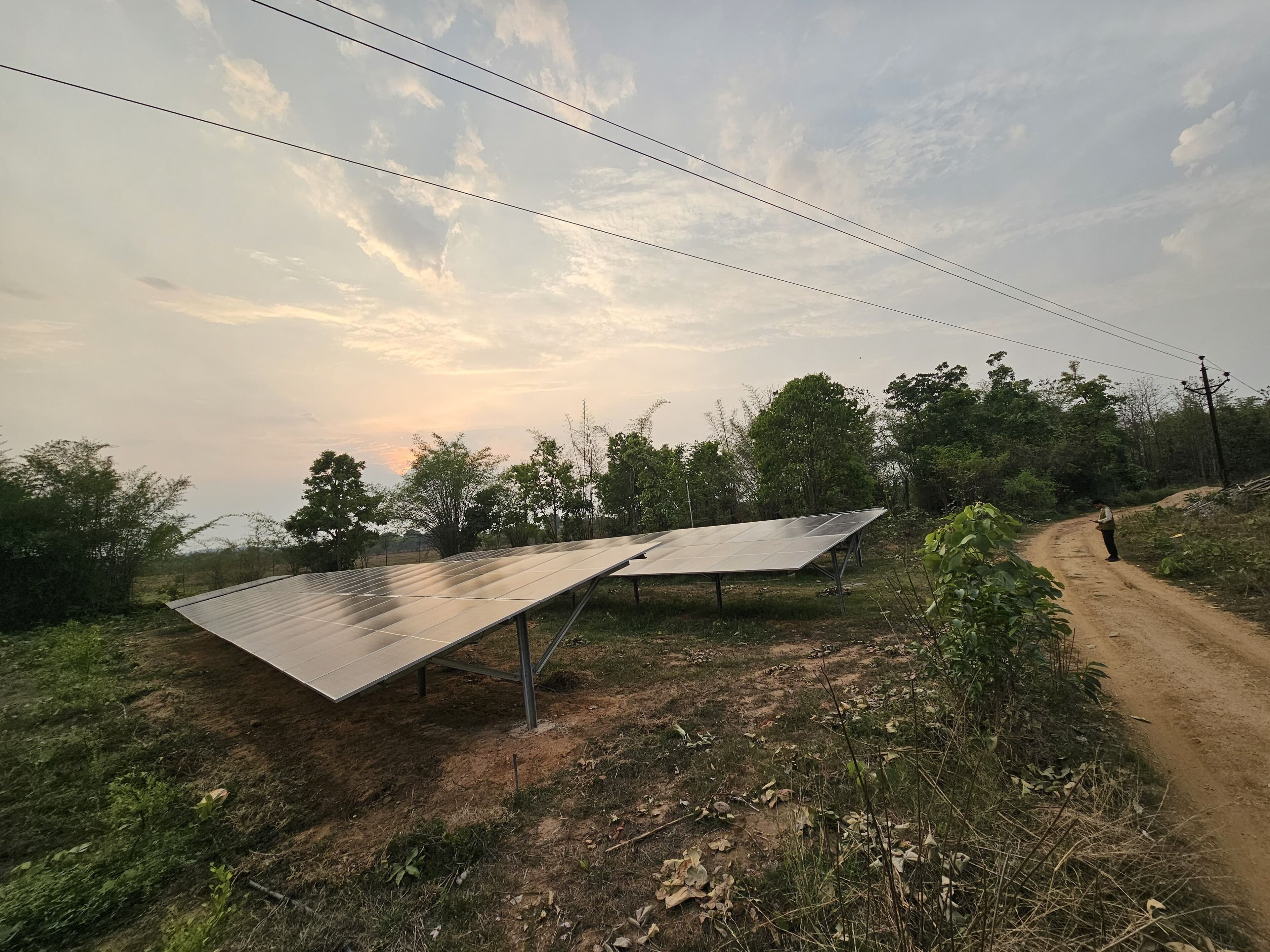 Solar panels installed on a rural dirt road with a person standing nearby.