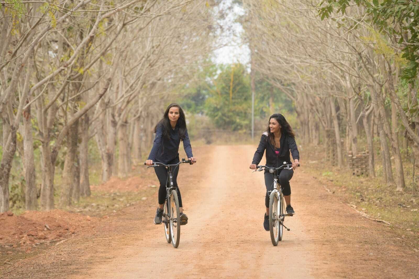 Two people riding bicycles on a dirt path surrounded by trees.