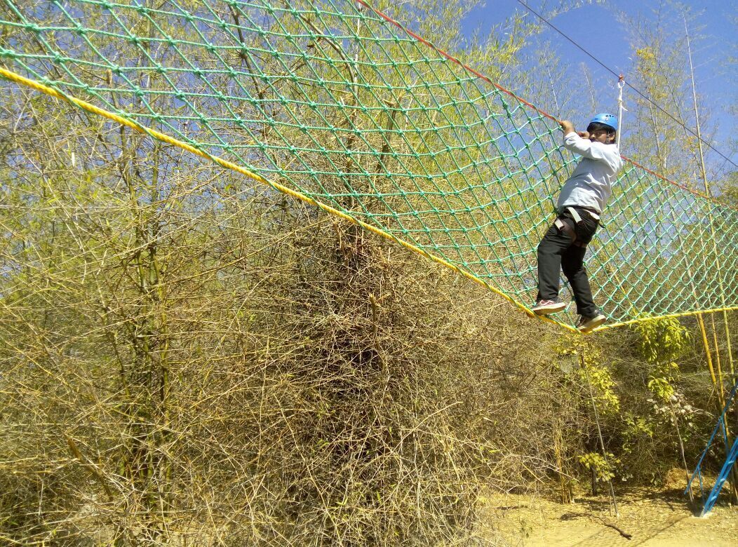 Una persona cruzando un puente colgante en un entorno natural.