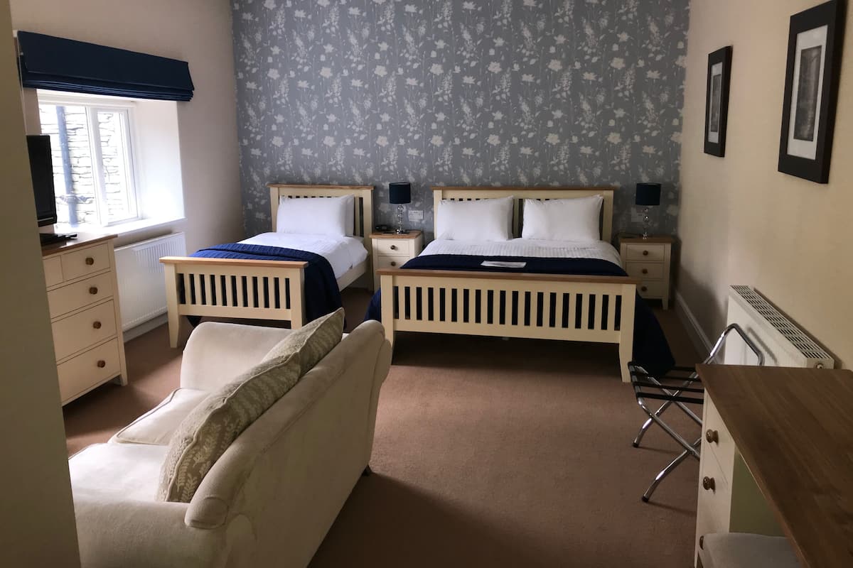 Une chambre avec deux lits simples, une commode en bois, une chaise, un radiateur et une fenêtre donnant sur un paysage agréable.