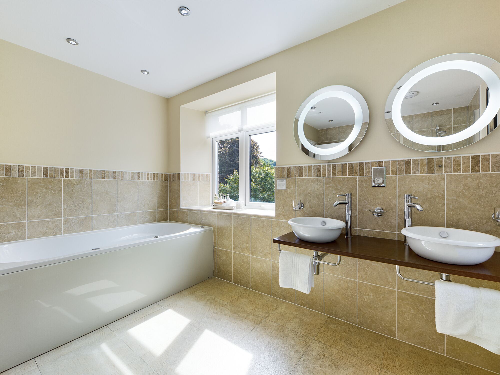 A modern bathroom with a bathtub, two sinks, and two wall-mounted mirrors.