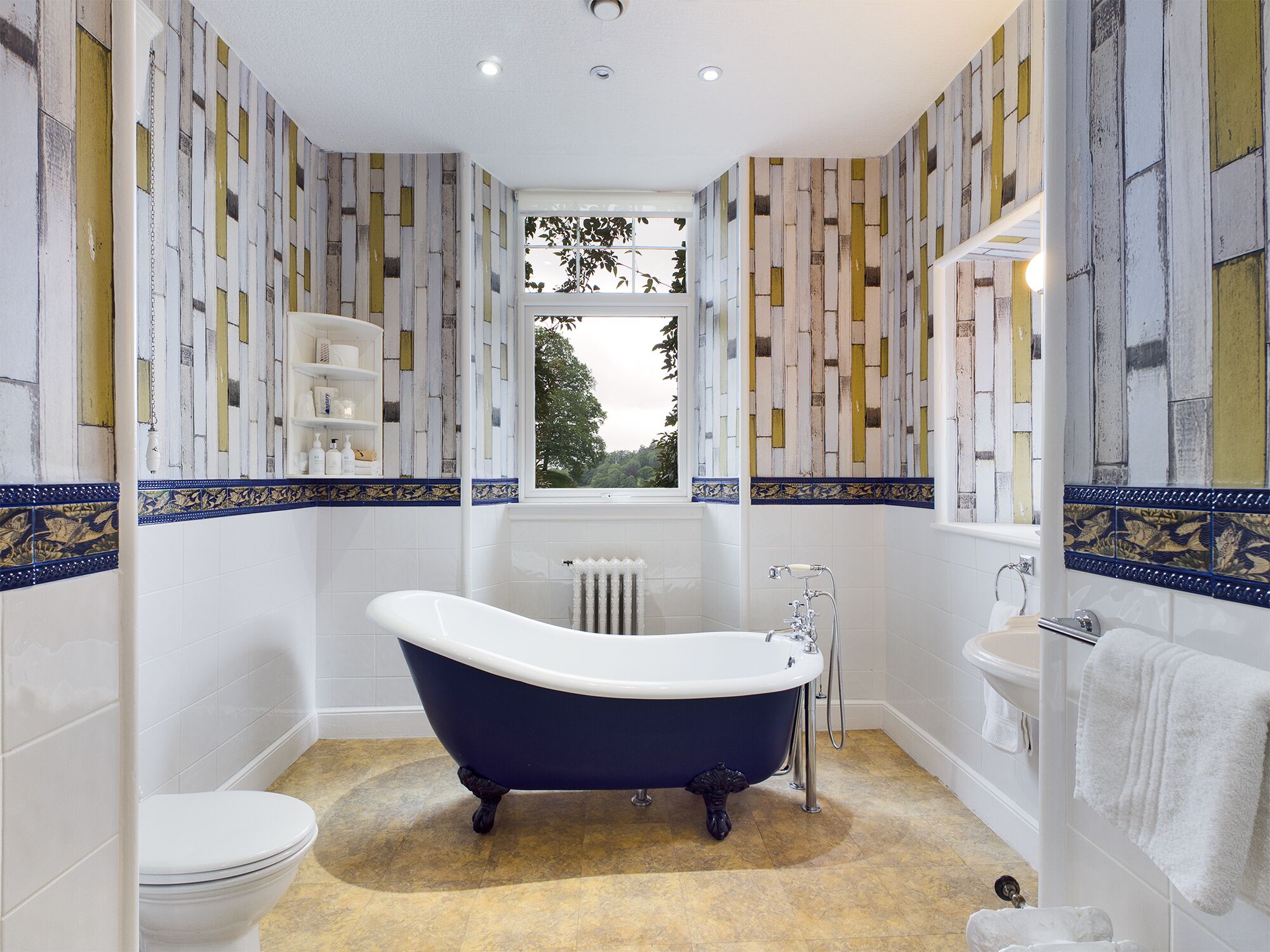 Un baño con una bañera independiente, azulejos blancos y un ventanal con vistas a zonas verdes.