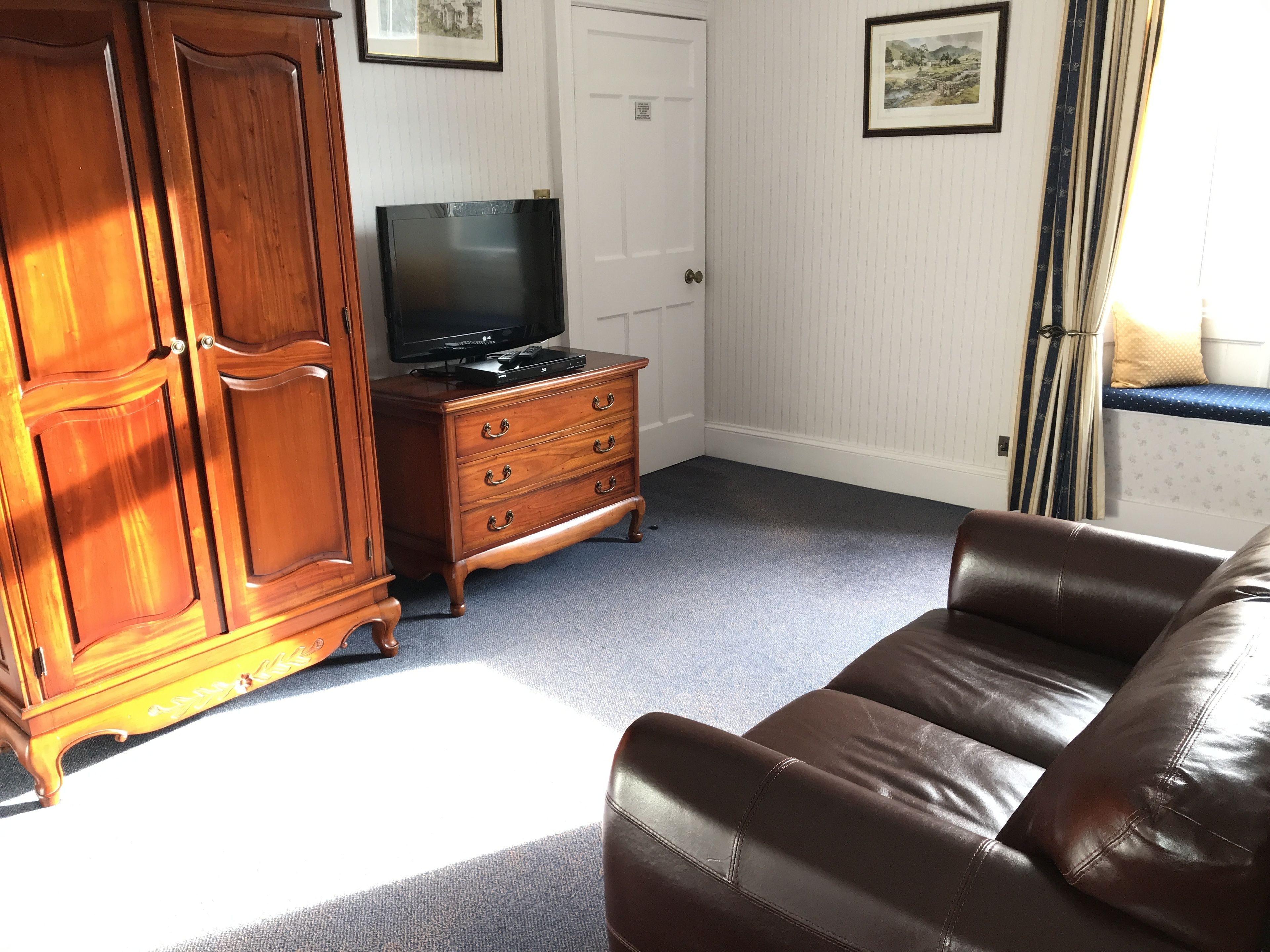 A room with a brown leather sofa, a wooden cabinet, a television on a stand, and a door.