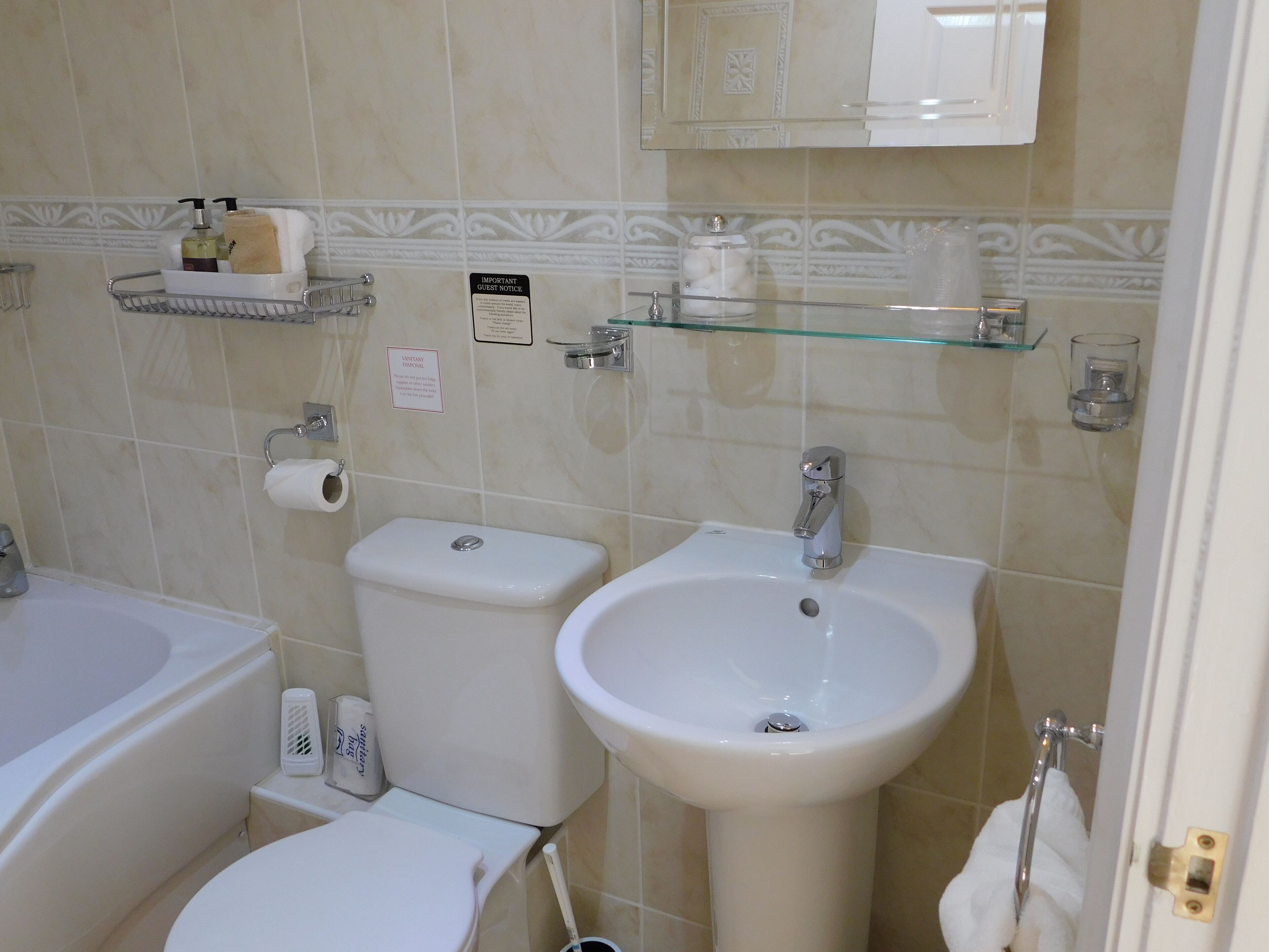 A bathroom with a toilet, bidet, sink, and glass shelves with toiletries.