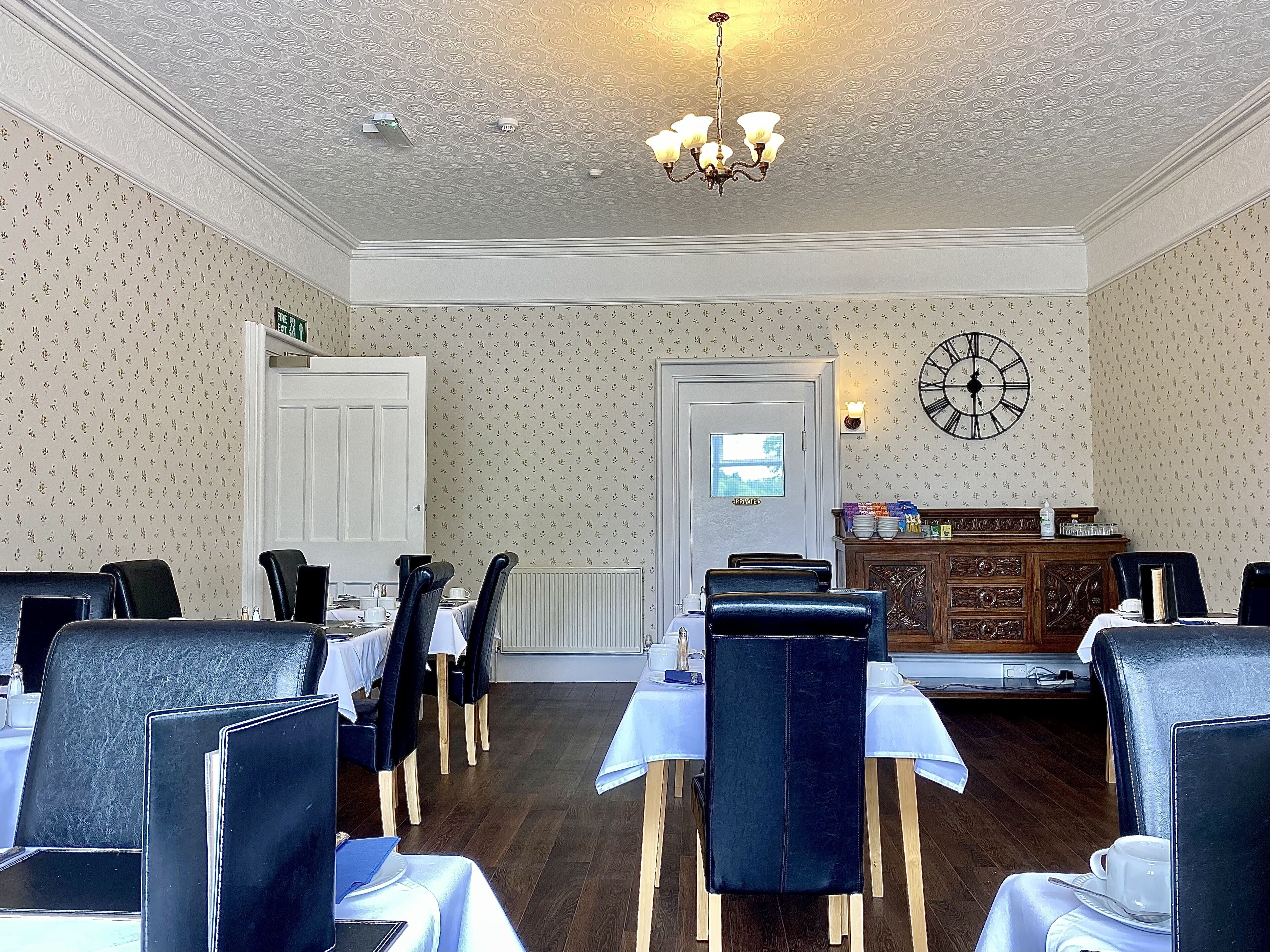 A dining area with tables set for four, a chandelier, a clock on the wall, and a view of the city through a window.