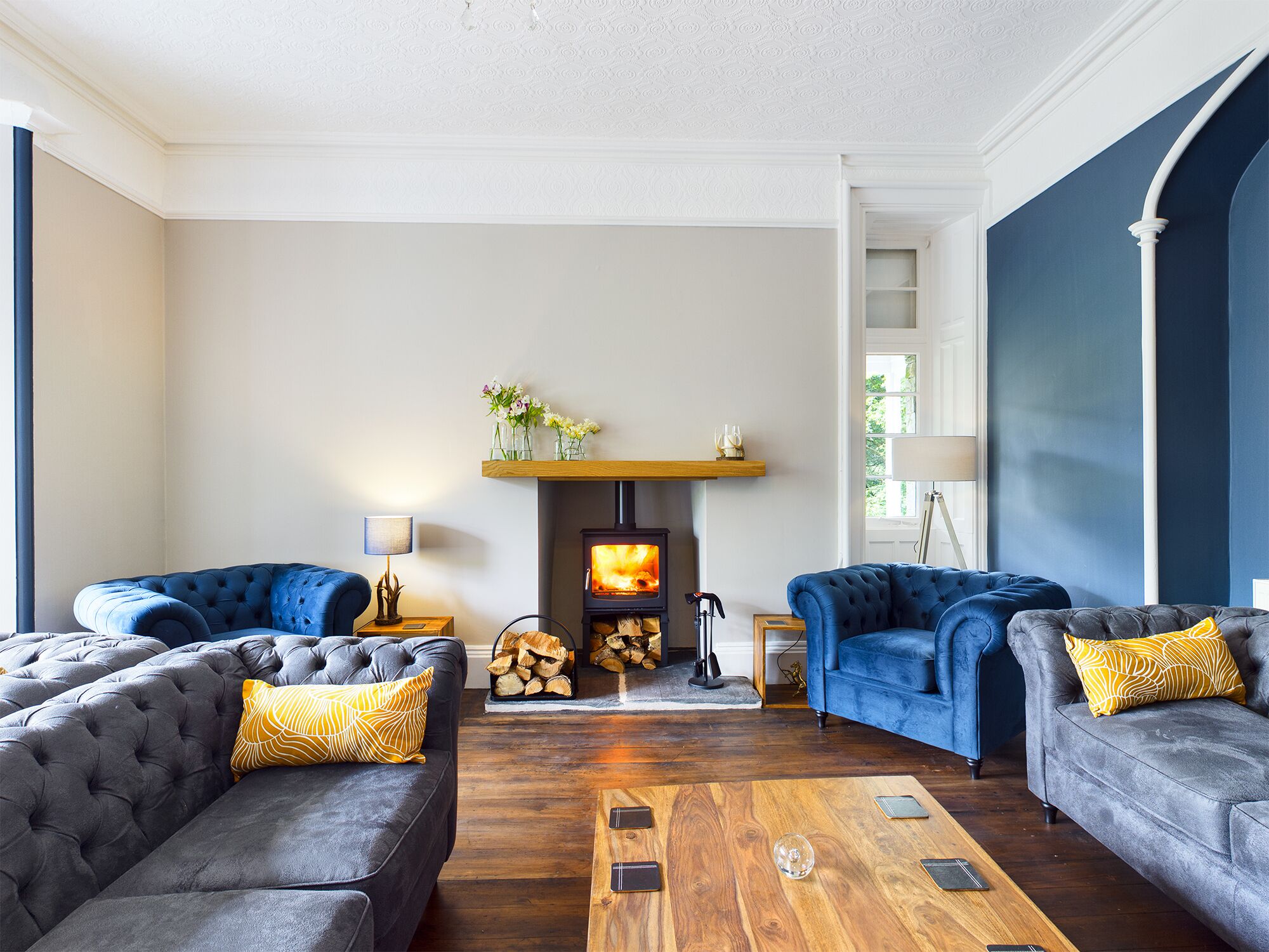 A living room with two grey sofas, a wooden coffee table, and a fireplace with a fire.