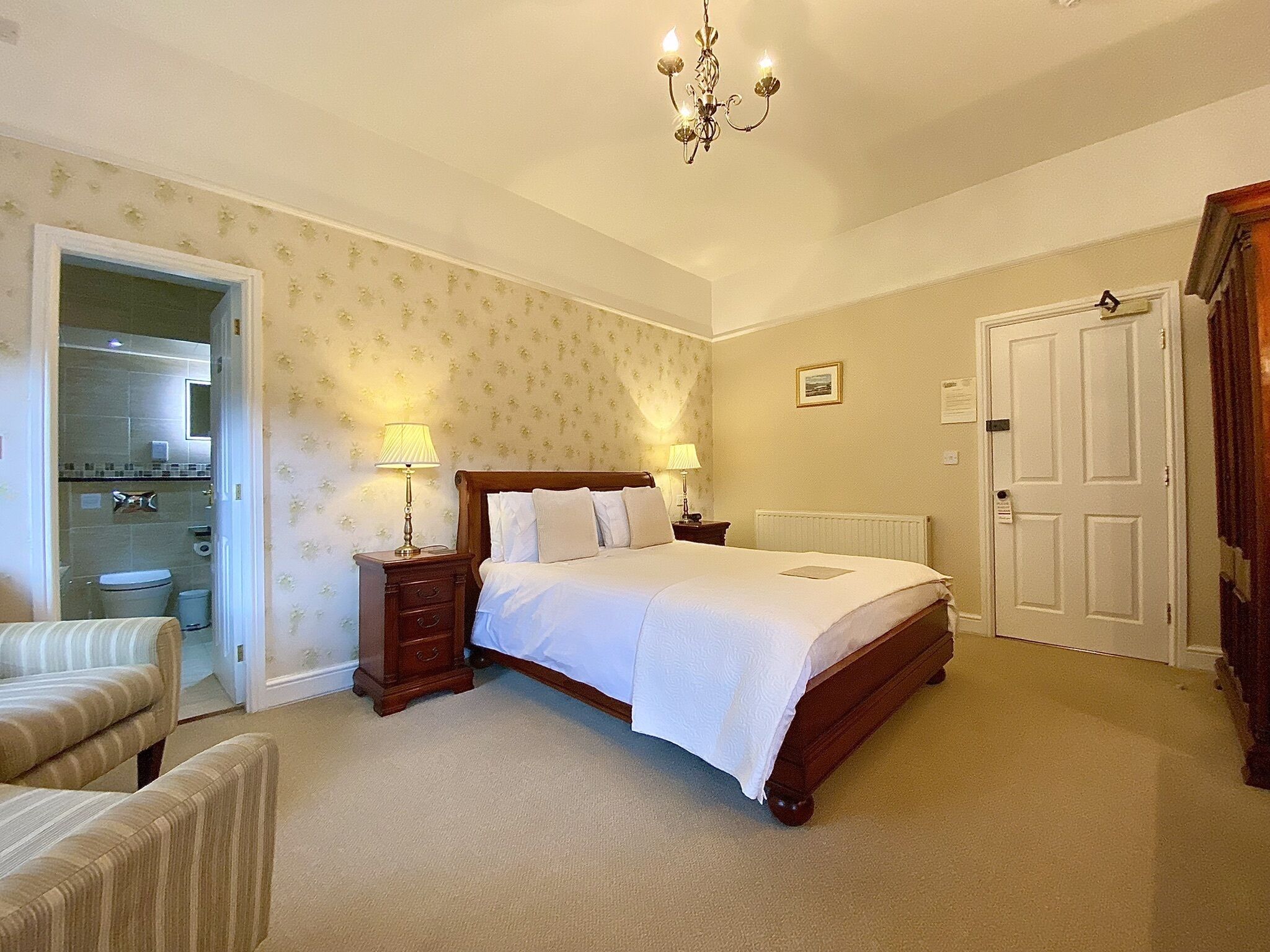 A bedroom with a bed, two bedside tables with lamps, a door, and a bathroom visible through an open door.