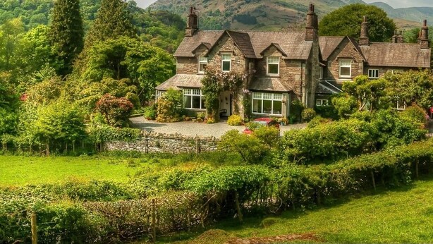 A stone house with multiple chimneys, surrounded by lush greenery and hills in the background. - Crow How Country Guest House (Ambleside)