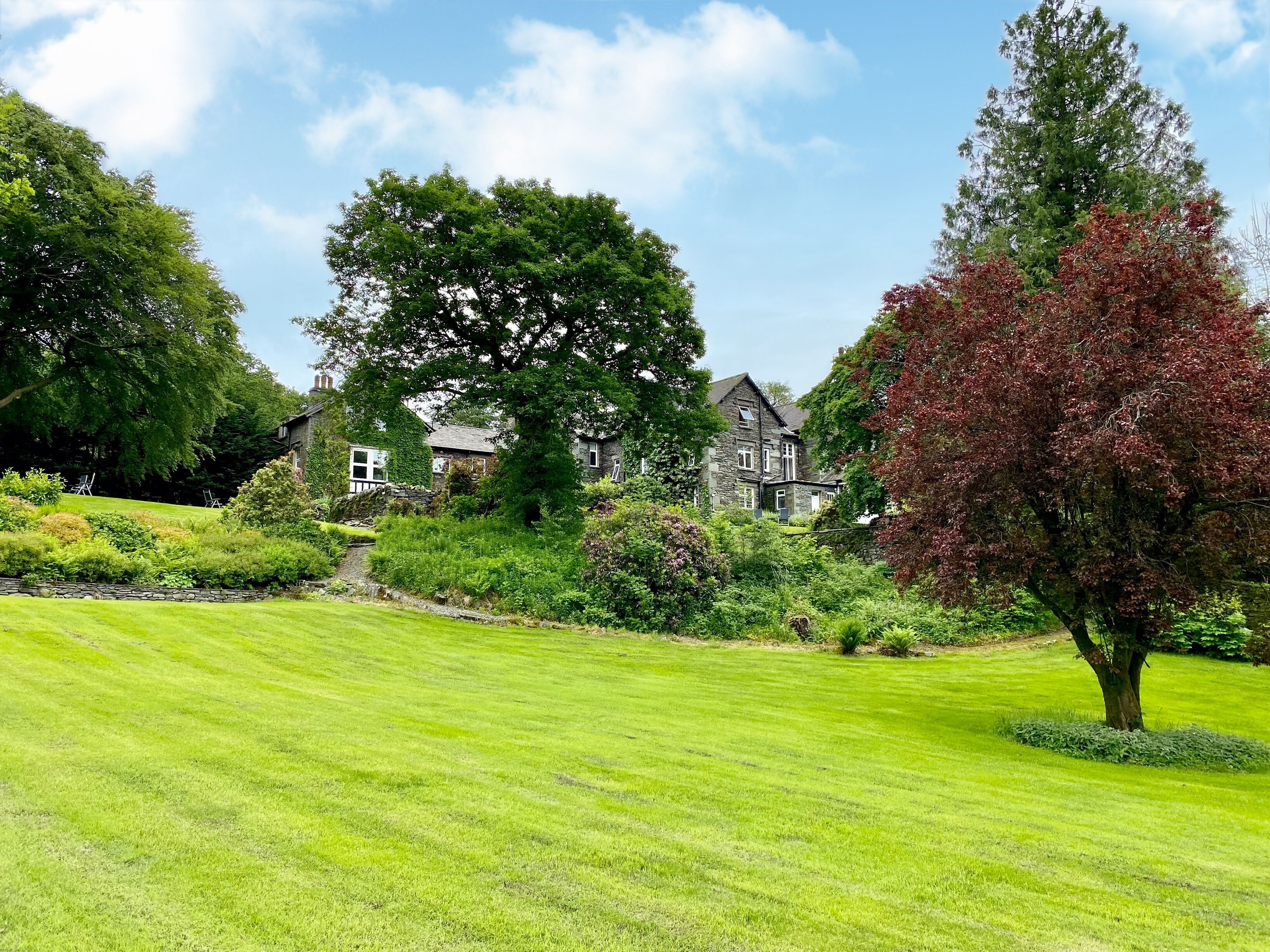A well-maintained lawn, a large tree, and a stone house with multiple windows.
