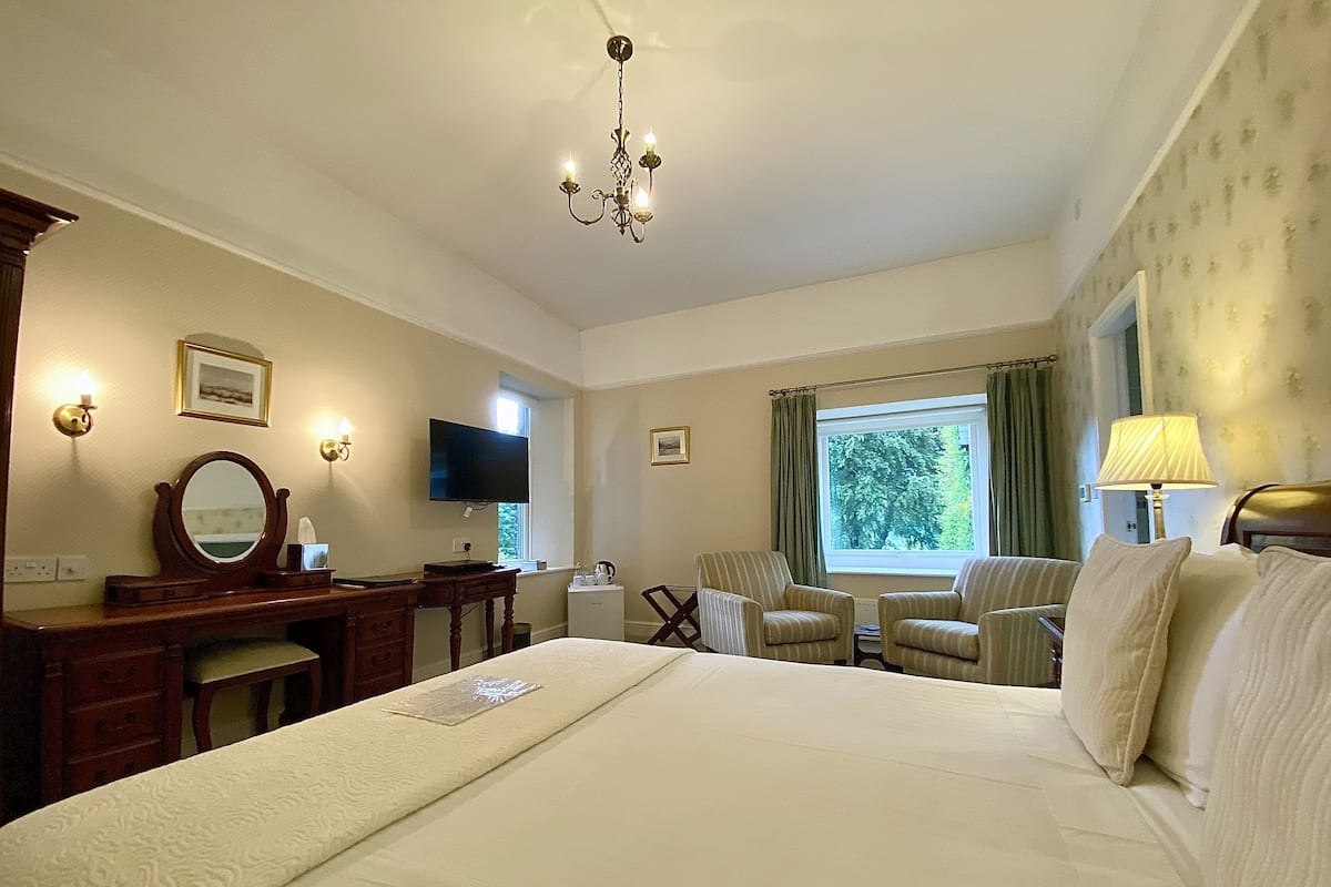 Une chambre d’hôtel avec un grand lit, un bureau avec une télévision, une chaise et une fenêtre avec des rideaux.