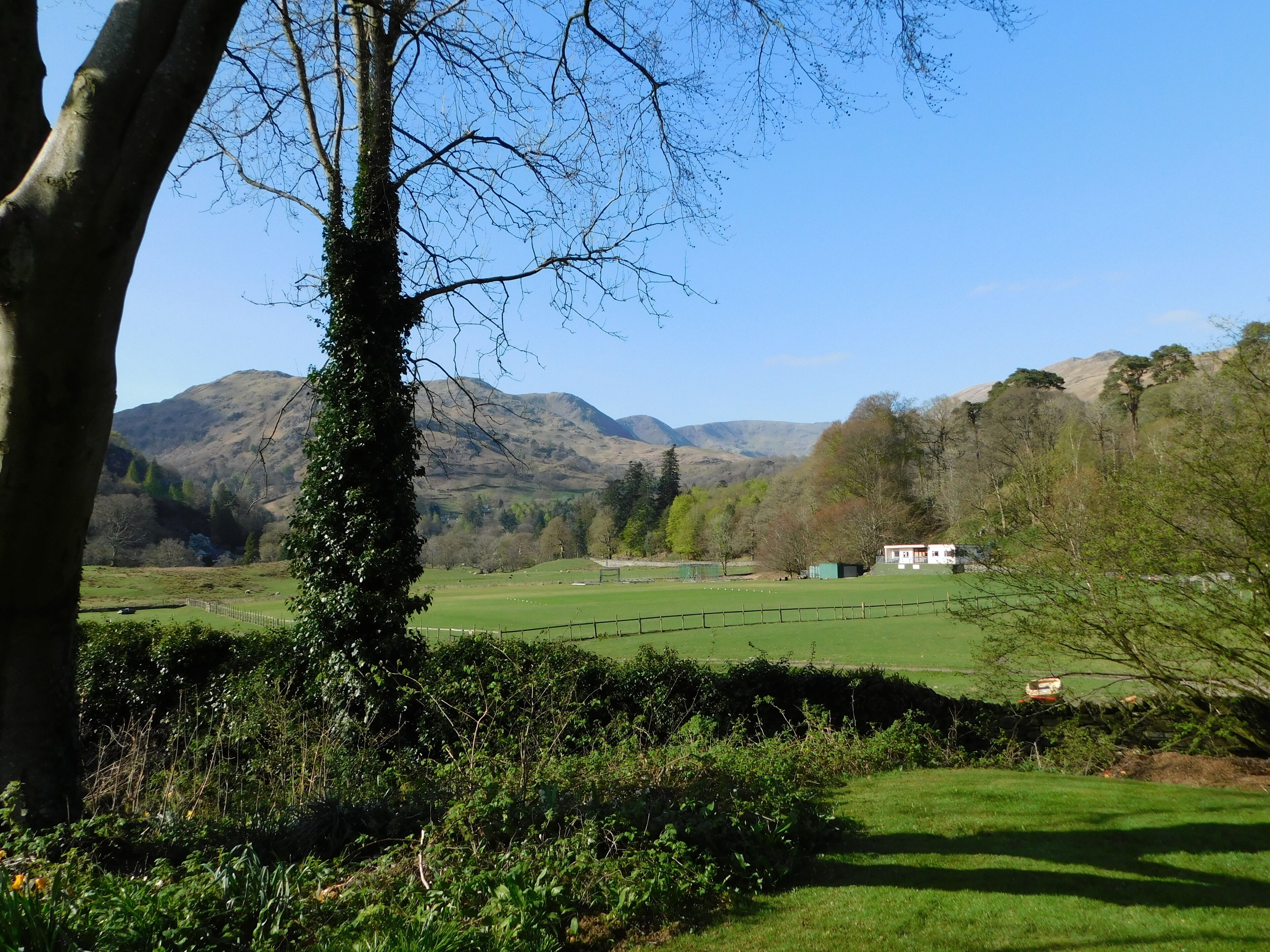 Un paysage rural avec une maison, des champs verdoyants et des montagnes en arrière-plan.