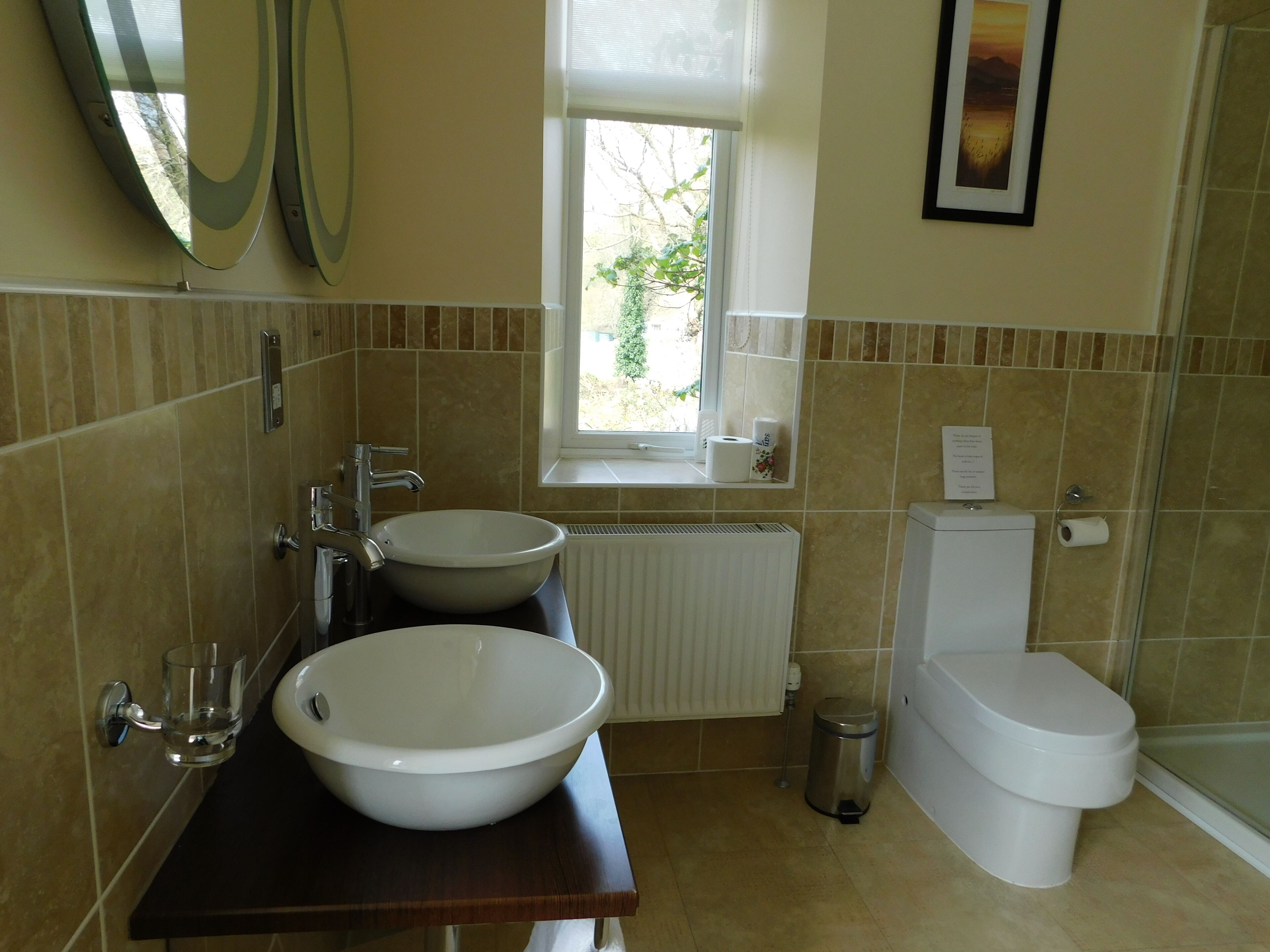 A bathroom with two sinks, a toilet, a window, and a radiator.