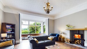 A spacious living room with a large sofa, a coffee table, and a fireplace. - Crow How Country Guest House (Ambleside)