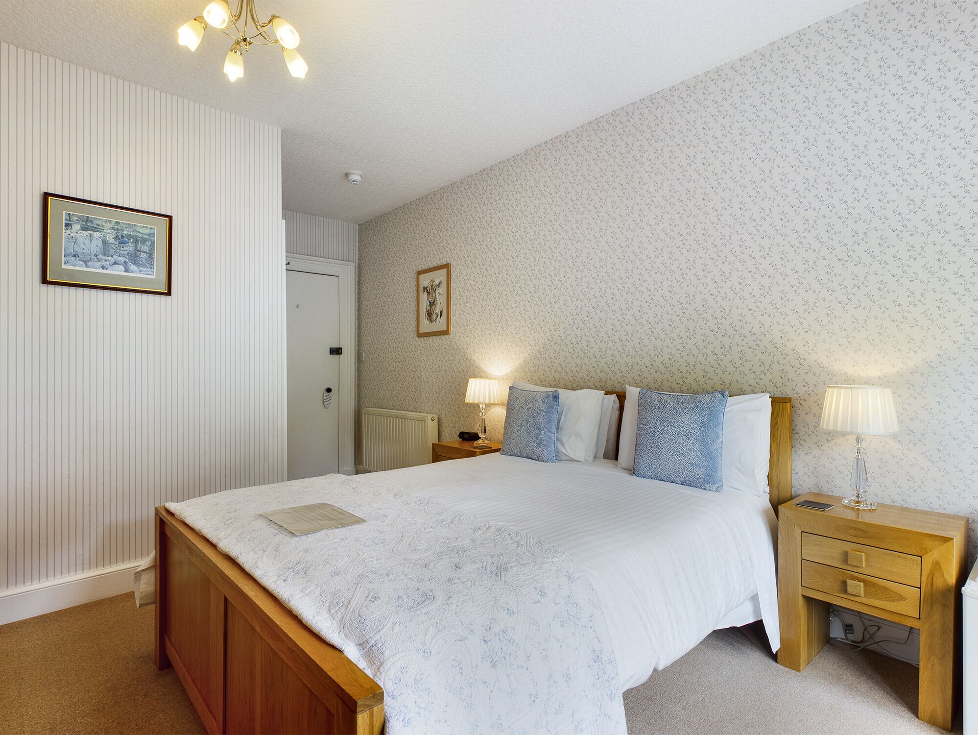 Une chambre avec un grand lit, une table de chevet en bois, deux lampes de chevet, un tableau encadré au mur et un radiateur.