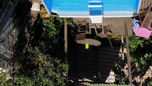 A swimming pool with a ladder and a chair, surrounded by a wooden deck and greenery.