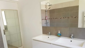 A bathroom with a double sink, a shower, and a glass-enclosed shower area.