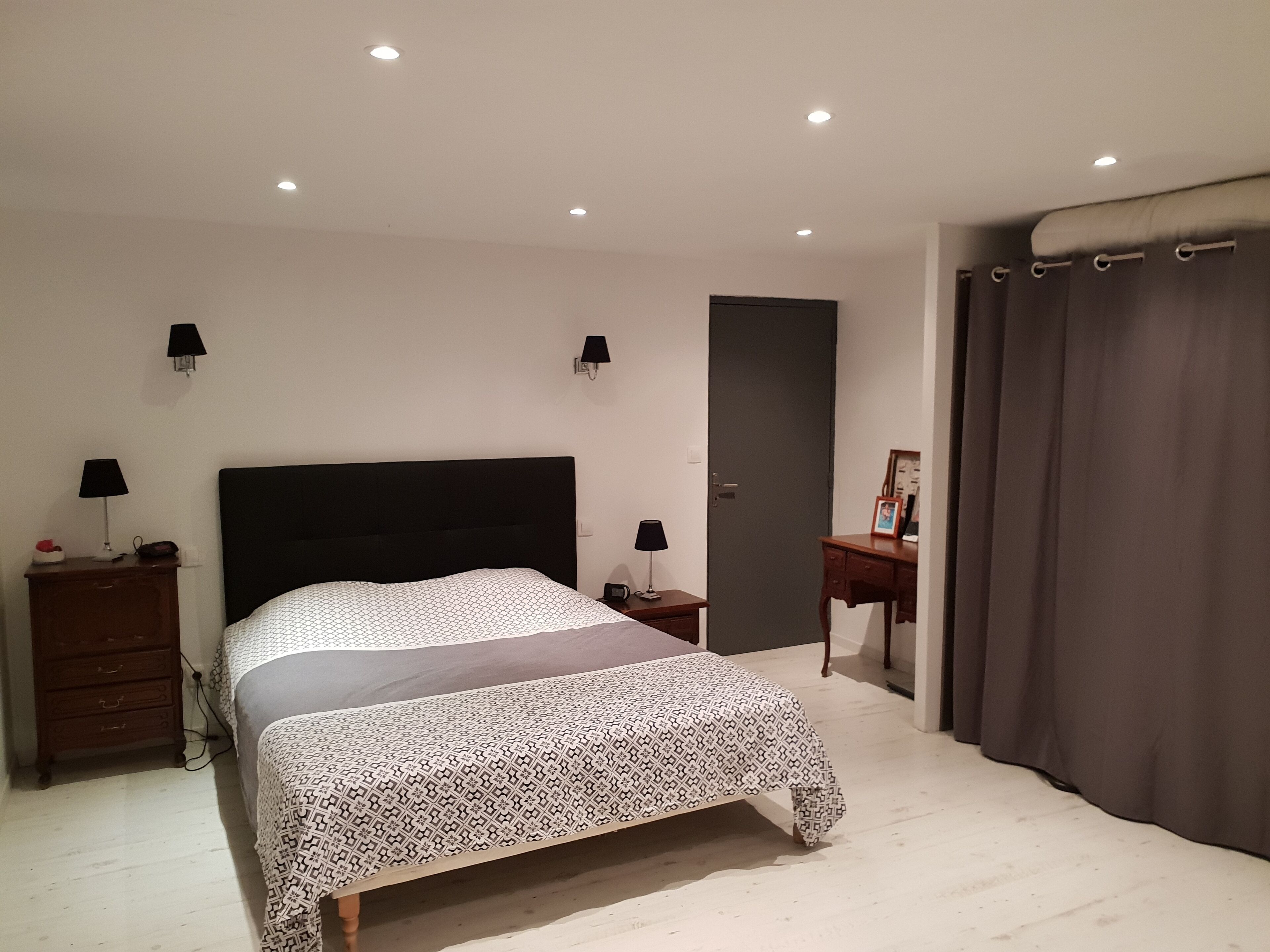Une chambre à coucher avec un lit, des tables de chevet, une commode, une porte et un rideau.