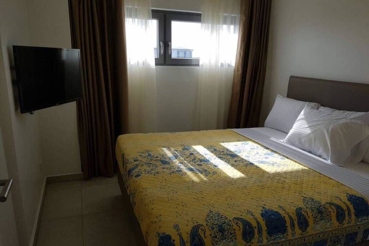 A hotel room with a bed, a flat-screen TV mounted on the wall, and a window with curtains.
