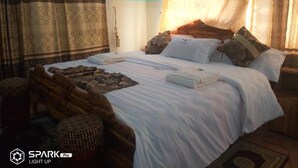 A neatly made bed with white linens and multiple pillows, a patterned rug, and traditional curtains. - Hotel Vilcabamba (Ho)