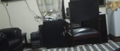 A room with a bed, a desk with a chair, a television, and a window with curtains.