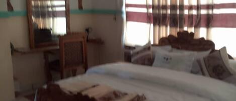 Une chambre avec un grand lit, un bureau, une chaise et une fenêtre avec des rideaux.