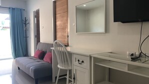 Una habitación moderna con un sofá gris, un escritorio blanco, un espejo y un televisor montado en la pared.