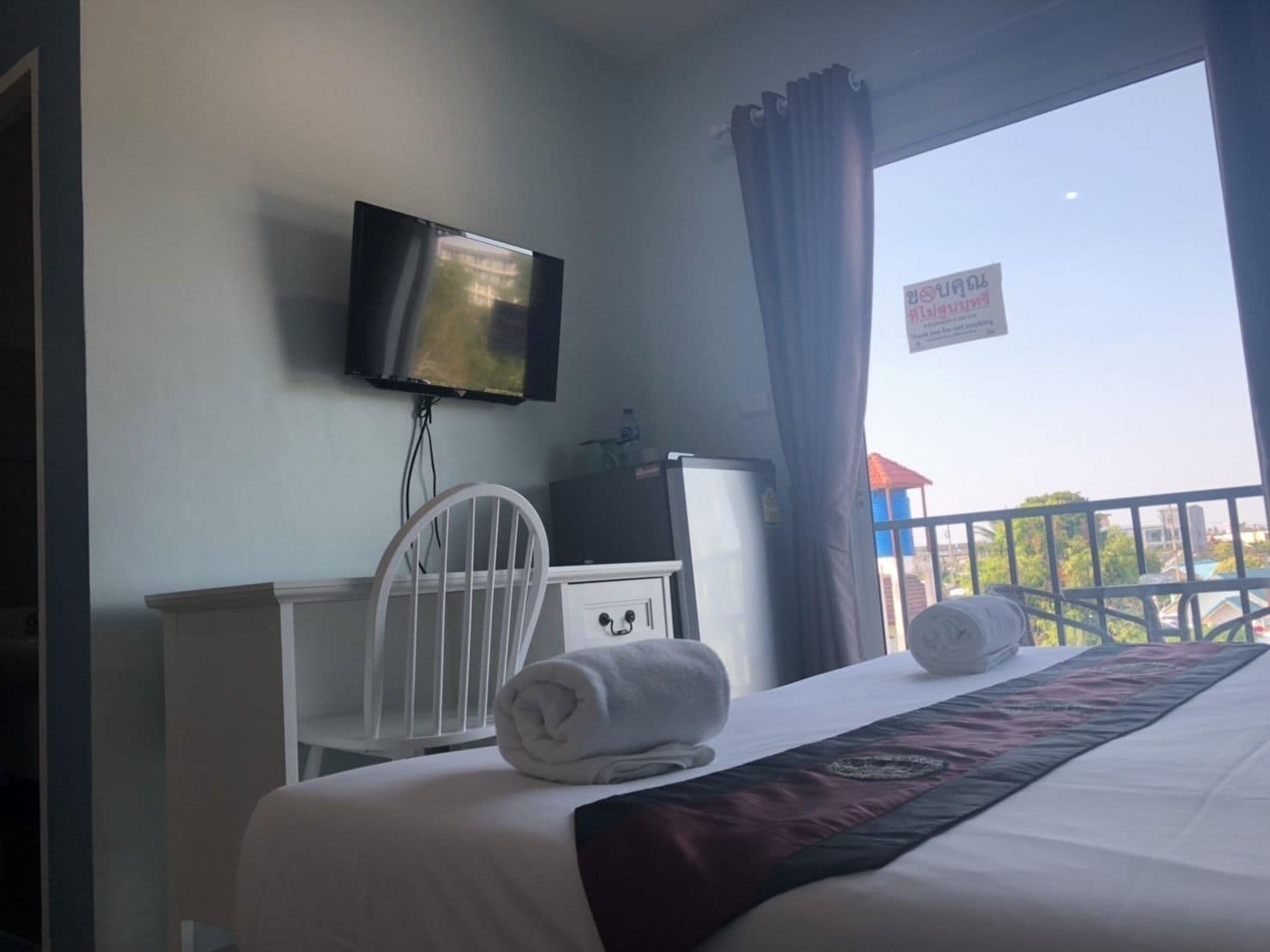 Ein Hotelzimmer mit Bett, einem an der Wand befestigten Fernseher, einem Schreibtisch mit Stuhl und einem Balkon mit Blick.