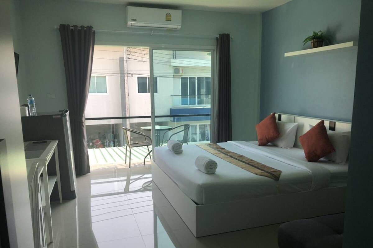 Een moderne hotelkamer met een groot bed, een balkon met een stoel en uitzicht op het gebouw.