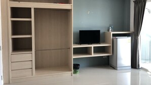 Un apartamento moderno con un armario de madera, un televisor de pantalla plana, un mini refrigerador y una pequeña cocina.