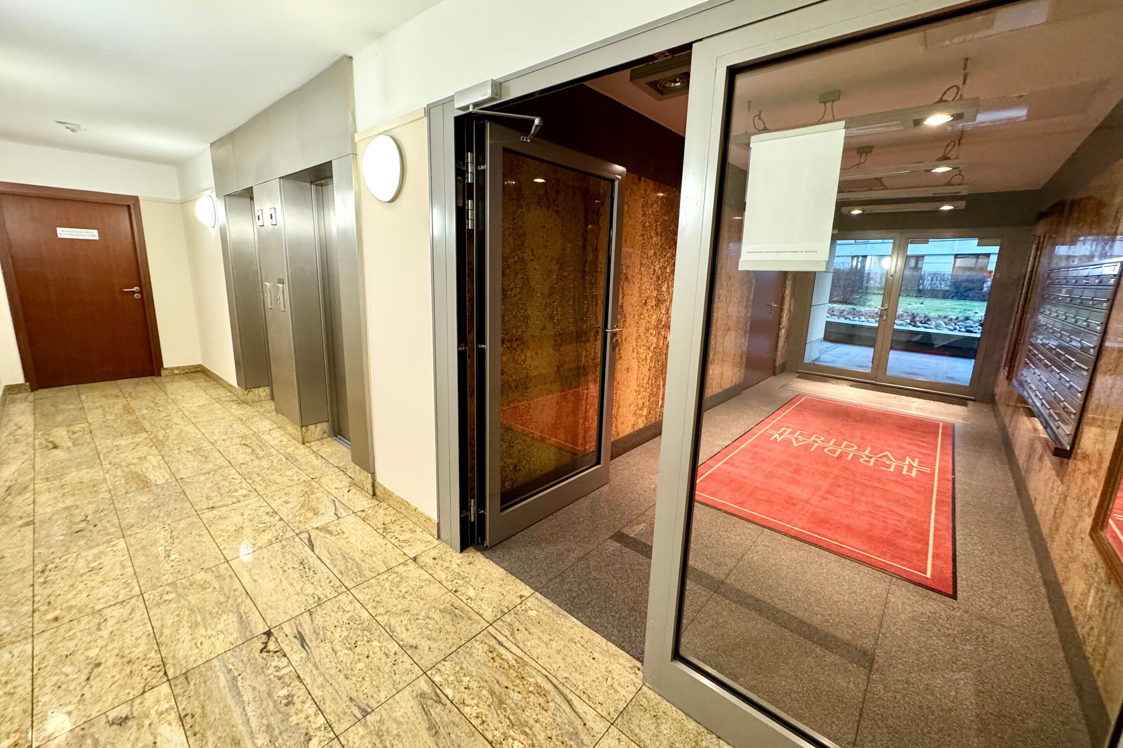 A hotel lobby with a marble floor, a red carpet, and a glass elevator.