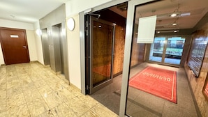 Un hall d’hôtel avec un sol en marbre, une moquette rouge et un ascenseur en verre.