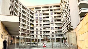 Un immeuble à plusieurs étages doté d’une façade incurvée, d’une entrée sécurisée par un portail et d’un panneau indiquant qu’il est interdit de se garer.