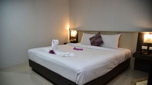 A neatly made bed with white linens, a wooden headboard, and a bedside table with a lamp. - Happy Room Hotel (Chiang Rai)