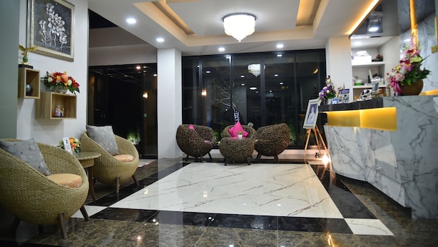 A hotel lobby with a marble reception desk, wicker chairs, a chandelier, and a large window. - Happy Room Hotel (Chiang Rai)