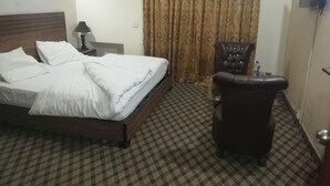 A hotel room with a bed, a chair, a checkered floor, an air conditioner, and a curtain. - Greenland Hotel (Lahore)