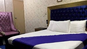 A hotel room with a large bed, a purple armchair, and a wooden nightstand. - Greenland Hotel (Lahore)