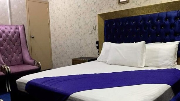 A hotel room with a large bed, a purple armchair, and a wooden nightstand. - Greenland Hotel (Lahore)