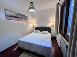 Een slaapkamer met een bed, een hanglamp, twee wandlampen, een raam met gordijnen en een radiator.